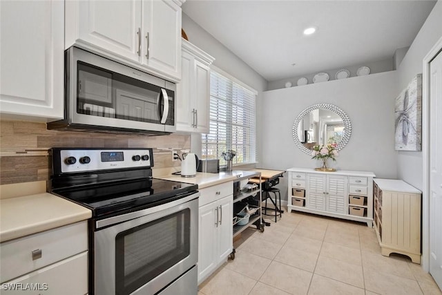 kitchen featuring light tile patterned flooring, stainless steel appliances, white cabinets, light countertops, and tasteful backsplash