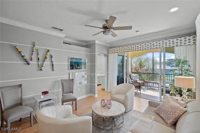 sitting room with a ceiling fan, visible vents, crown molding, and wood finished floors