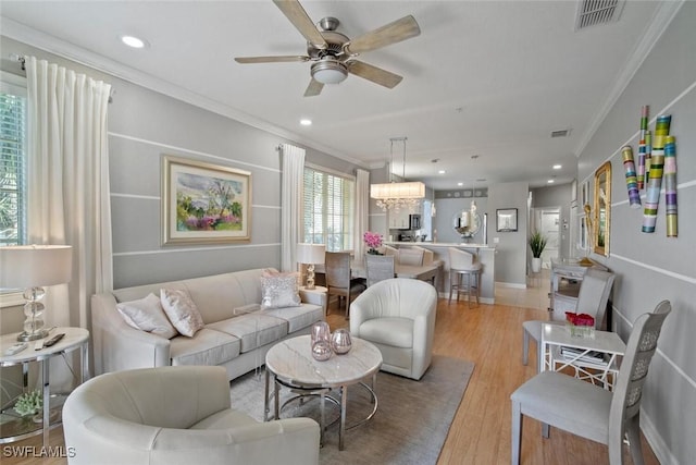 living area with crown molding, recessed lighting, visible vents, light wood-style floors, and ceiling fan with notable chandelier