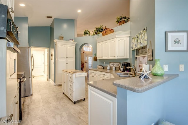 kitchen with arched walkways, recessed lighting, white cabinets, a sink, and a peninsula