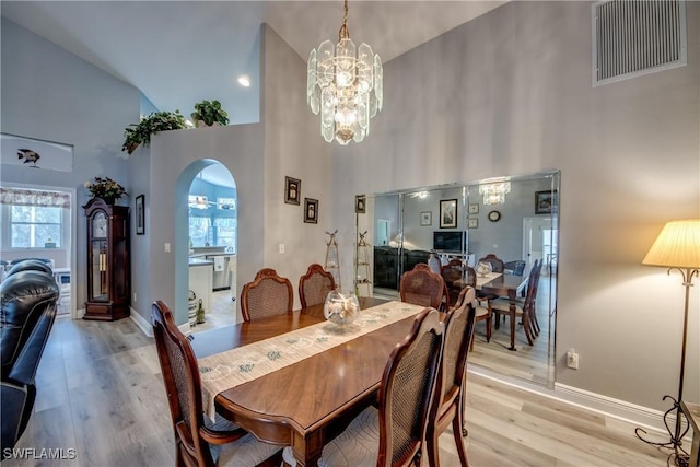 dining room featuring light wood-type flooring, a towering ceiling, visible vents, and arched walkways