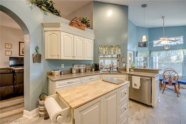 kitchen with arched walkways, stainless steel dishwasher, white cabinets, a sink, and a peninsula