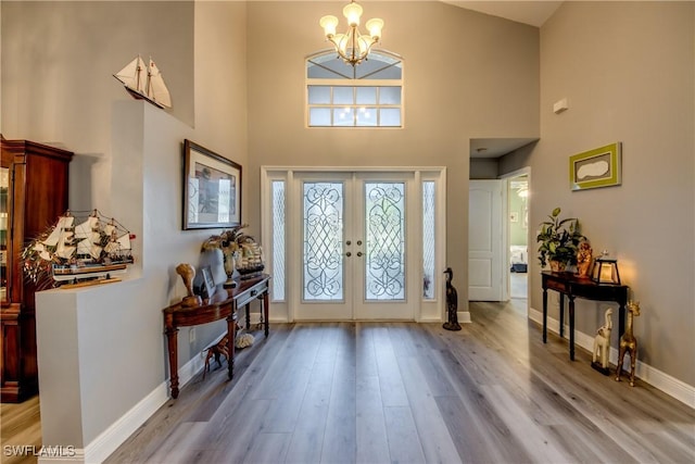 entrance foyer with french doors, a notable chandelier, a high ceiling, wood finished floors, and baseboards