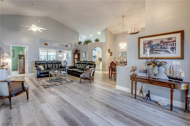 living area featuring arched walkways, baseboards, a ceiling fan, light wood-style flooring, and high vaulted ceiling