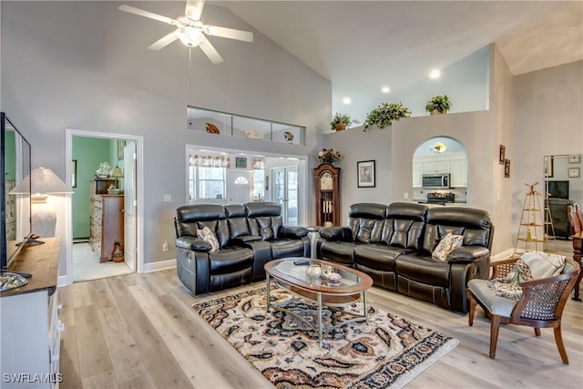 living area featuring light wood-style floors, baseboards, high vaulted ceiling, and a ceiling fan