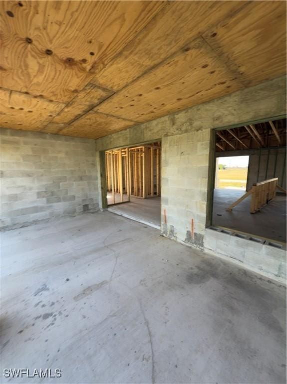 interior space featuring concrete block wall, wood ceiling, and unfinished concrete floors