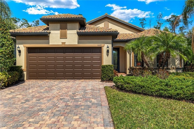 mediterranean / spanish-style house featuring an attached garage, a tile roof, decorative driveway, and stucco siding