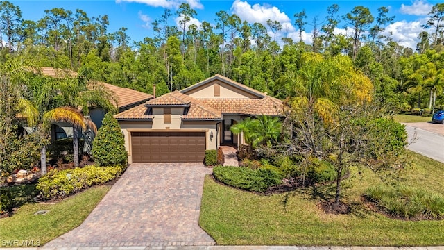 mediterranean / spanish-style home with an attached garage, stucco siding, decorative driveway, and a tiled roof