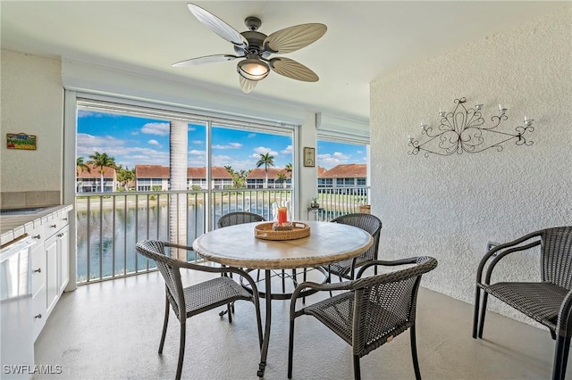 dining space featuring a textured wall, a water view, and ceiling fan