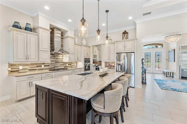 kitchen with a spacious island, stainless steel appliances, french doors, wall chimney range hood, and a sink