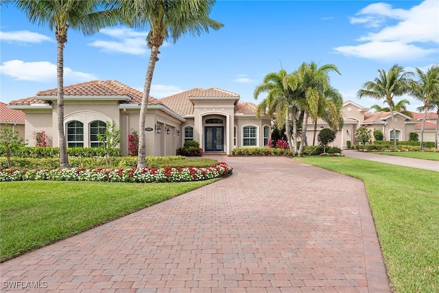 mediterranean / spanish-style house featuring a front yard, decorative driveway, a tile roof, and stucco siding