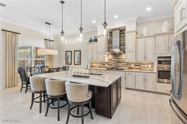 kitchen featuring stainless steel appliances, backsplash, wall chimney exhaust hood, a kitchen bar, and crown molding