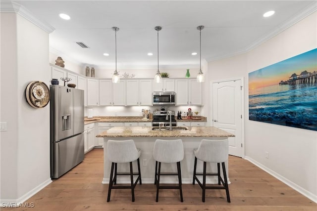 kitchen featuring light wood finished floors, appliances with stainless steel finishes, a kitchen breakfast bar, ornamental molding, and a sink