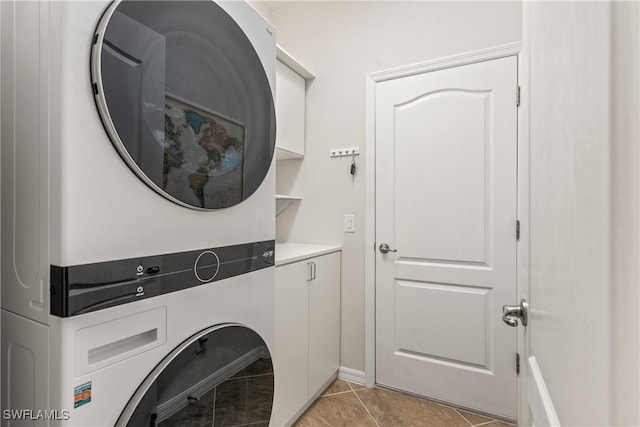 laundry room featuring light tile patterned floors, stacked washing maching and dryer, and cabinet space