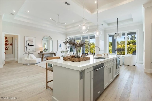 kitchen with visible vents, dishwasher, light wood-style flooring, a tray ceiling, and a sink