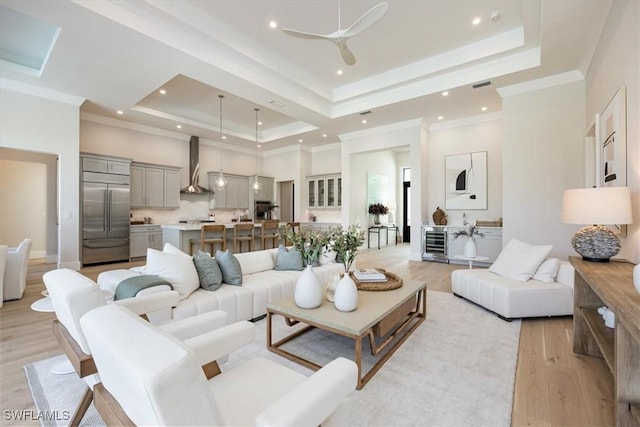 living area with ornamental molding, a tray ceiling, wine cooler, and light wood-style floors