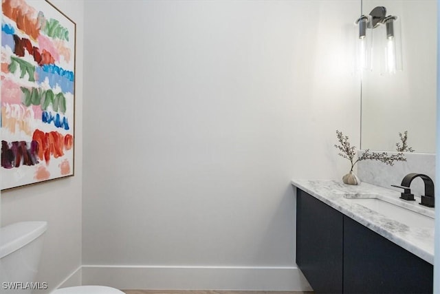 half bathroom featuring toilet, baseboards, and vanity