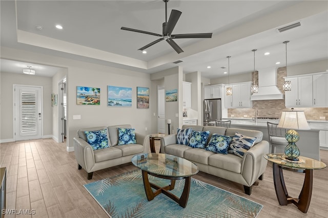 living area featuring baseboards, a tray ceiling, visible vents, and light wood-style floors