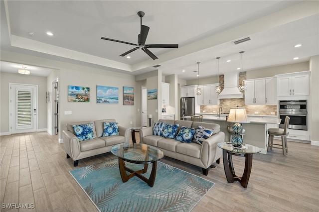 living room with light wood finished floors, baseboards, visible vents, and a raised ceiling