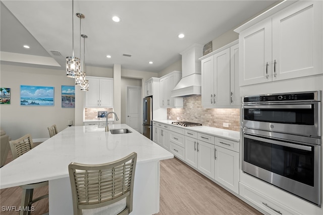 kitchen featuring light wood finished floors, visible vents, appliances with stainless steel finishes, a sink, and premium range hood