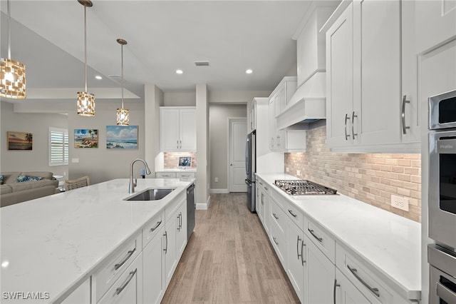 kitchen featuring appliances with stainless steel finishes, open floor plan, white cabinets, a sink, and light wood-type flooring