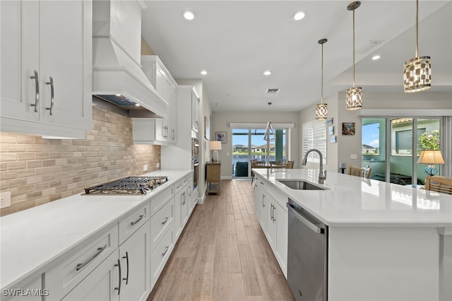 kitchen featuring stainless steel appliances, a sink, white cabinetry, backsplash, and custom range hood