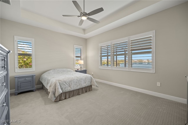 bedroom with a raised ceiling, light colored carpet, visible vents, ceiling fan, and baseboards