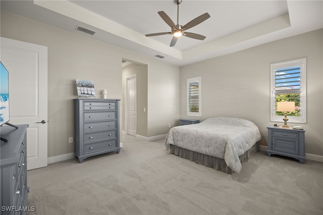 bedroom featuring visible vents, baseboards, light colored carpet, ceiling fan, and a tray ceiling