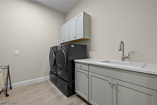 clothes washing area featuring cabinet space, baseboards, independent washer and dryer, light wood-type flooring, and a sink