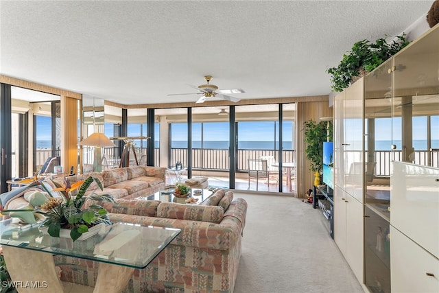 living area with light carpet, ceiling fan, expansive windows, and a textured ceiling