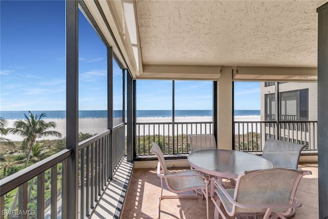 sunroom featuring a water view and a beach view