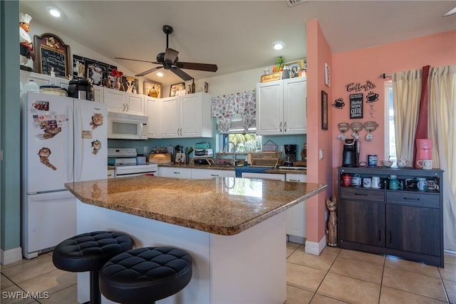 kitchen featuring white appliances, light tile patterned floors, dark stone counters, a kitchen island, and white cabinetry