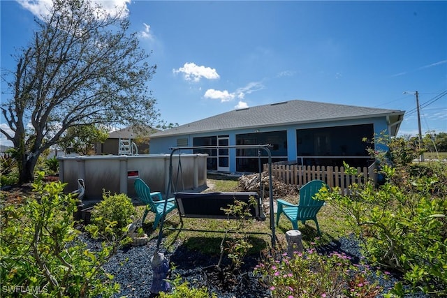 rear view of property featuring an outdoor pool, a sunroom, and fence