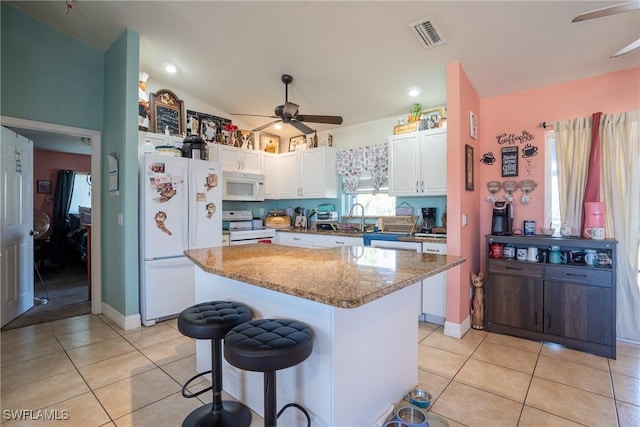 kitchen with light tile patterned floors, a breakfast bar area, white appliances, visible vents, and white cabinetry