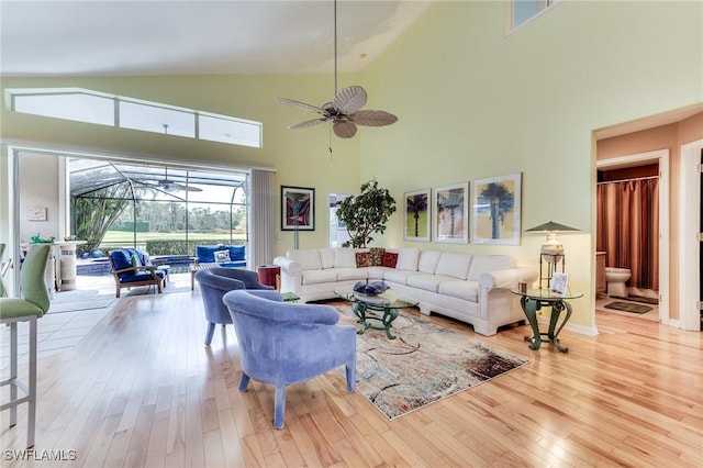 living area with a sunroom, wood-type flooring, high vaulted ceiling, and a ceiling fan