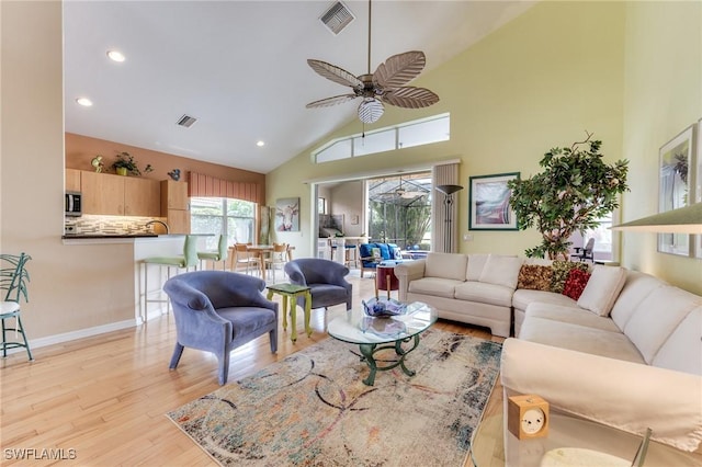 living area with high vaulted ceiling, light wood finished floors, visible vents, and a ceiling fan