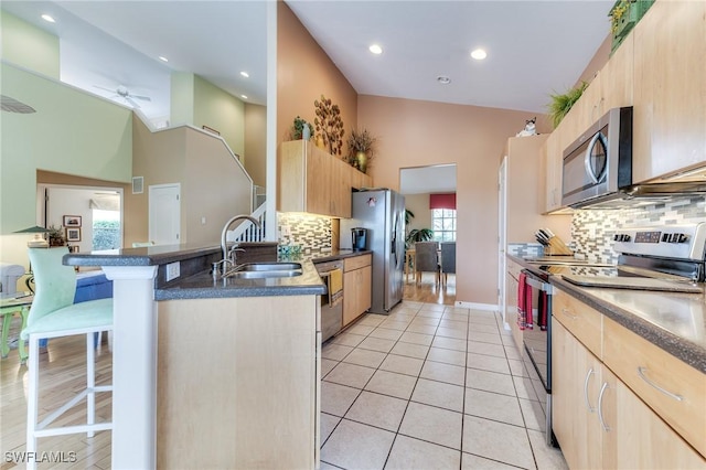 kitchen featuring light tile patterned floors, appliances with stainless steel finishes, a breakfast bar, and light brown cabinetry