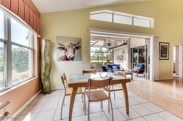 dining room featuring light tile patterned floors, high vaulted ceiling, a ceiling fan, and baseboards