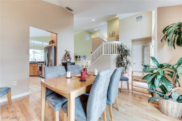 dining room featuring stairs, light wood finished floors, a high ceiling, and visible vents