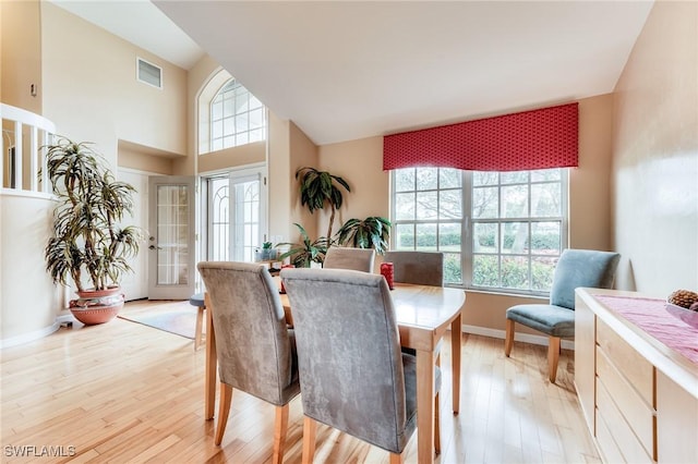 dining area with baseboards, high vaulted ceiling, visible vents, and light wood-style floors