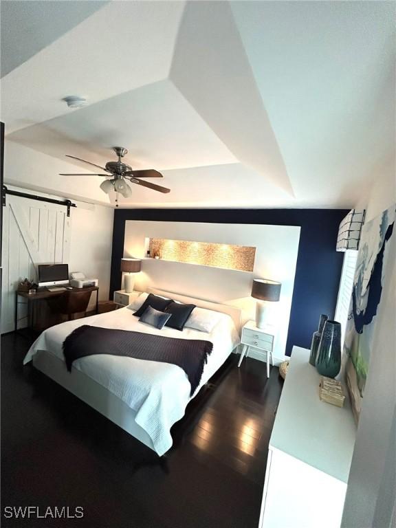 bedroom with a ceiling fan, a barn door, and dark wood-style floors