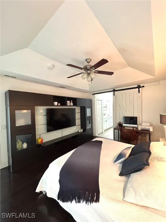 bedroom featuring visible vents, ceiling fan, lofted ceiling, a tray ceiling, and a barn door