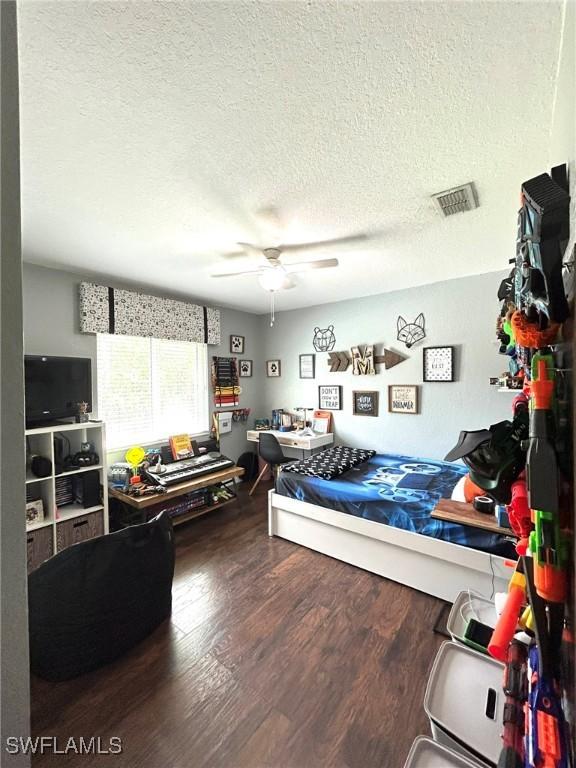 bedroom featuring a ceiling fan, wood finished floors, visible vents, and a textured ceiling