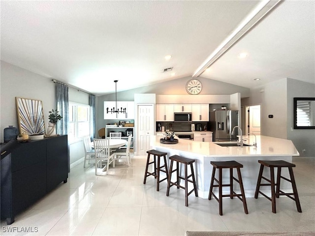 kitchen featuring light countertops, a kitchen bar, lofted ceiling with beams, appliances with stainless steel finishes, and white cabinets