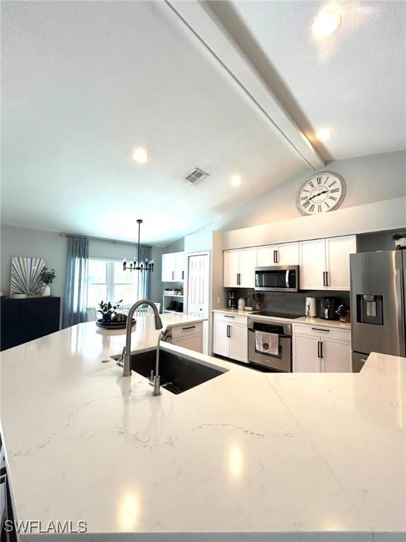 kitchen featuring visible vents, lofted ceiling with beams, appliances with stainless steel finishes, white cabinetry, and a sink