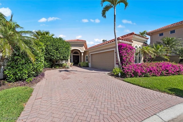 mediterranean / spanish-style home featuring a garage, decorative driveway, a tile roof, and stucco siding