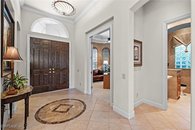 foyer entrance featuring light tile patterned floors, baseboards, ornamental molding, and a wealth of natural light