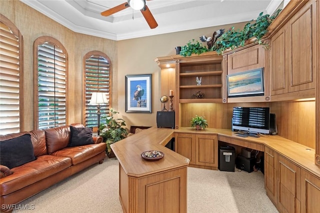 office space featuring light carpet, a ceiling fan, ornamental molding, a tray ceiling, and built in desk