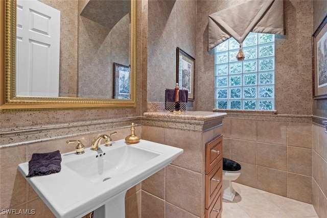 half bath with tile walls, toilet, a wainscoted wall, tile patterned flooring, and a sink