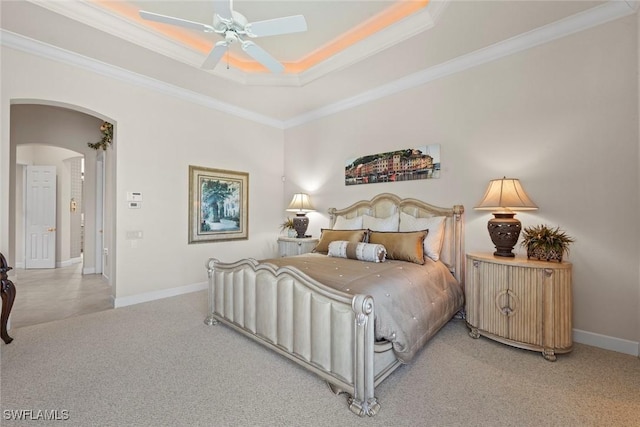 carpeted bedroom featuring arched walkways, a raised ceiling, ornamental molding, a ceiling fan, and baseboards